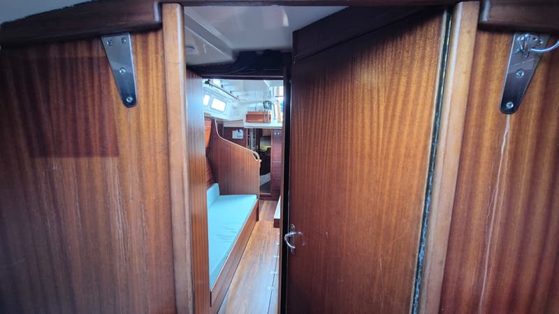 Een doorkijkje in de kajuit van een boot met houten wanden en een lichtblauw kussen op een bank. — Contest 36 Ketch