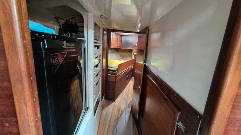Een gangpad in een boot met een LG koelkast, houten vloer en een open deur naar een slaapruimte. — Contest 36 Ketch