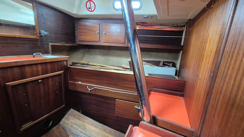 De foto toont het interieur van een bootkajuit met houten panelen, een spiegel, opbergruimte en een trap met oranje…