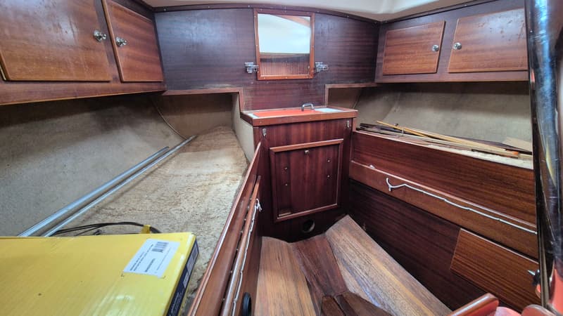 De foto toont een kajuit met houten wanden, kasten, een spiegel en een gele doos op een stoffen bank. — Contest 36 Ketch