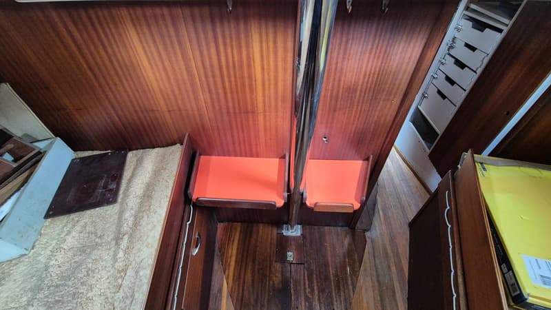 De foto toont een interieur van een boot met houten wanden en vloer, twee oranje stoelen en een metalen paal.