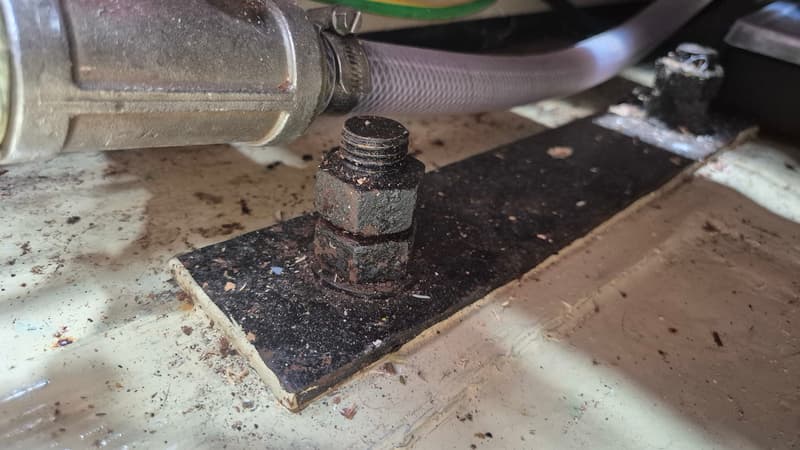Een detailopname van een metalen bout en moer op een donkere plaat, met een slang en klem op de achtergrond.
