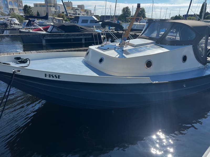 Een blauw-witte boot met de naam "HISSE" op de boeg ligt in het water, met zonnepanelen en een donkere kap.