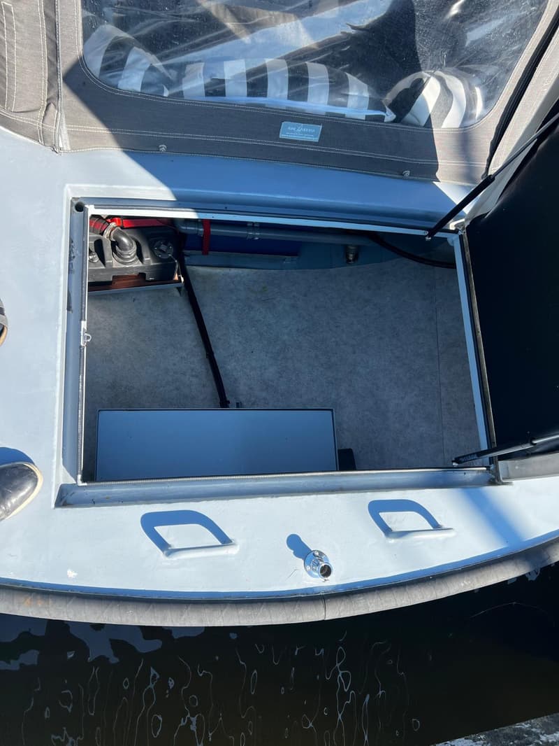 Een open compartiment in een lichtgrijze boot toont een zwarte tank, blauwe leidingen, een grijze box en een lichtgrijze…