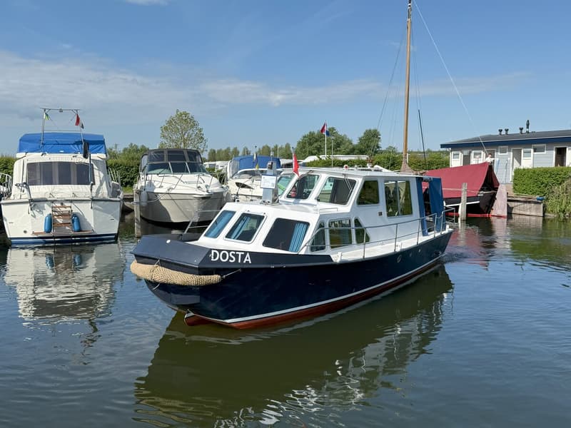 Een blauw-witte boot met de naam "DOSTA" ligt in het water, omringd door andere boten en gebouwen. — Beachcraft 850 Refit