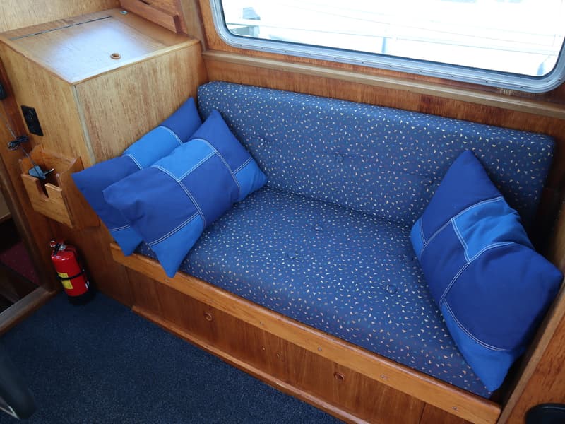 Een blauwe bank met patroon en drie blauwe kussens in een houten interieur met een raam en een brandblusser.