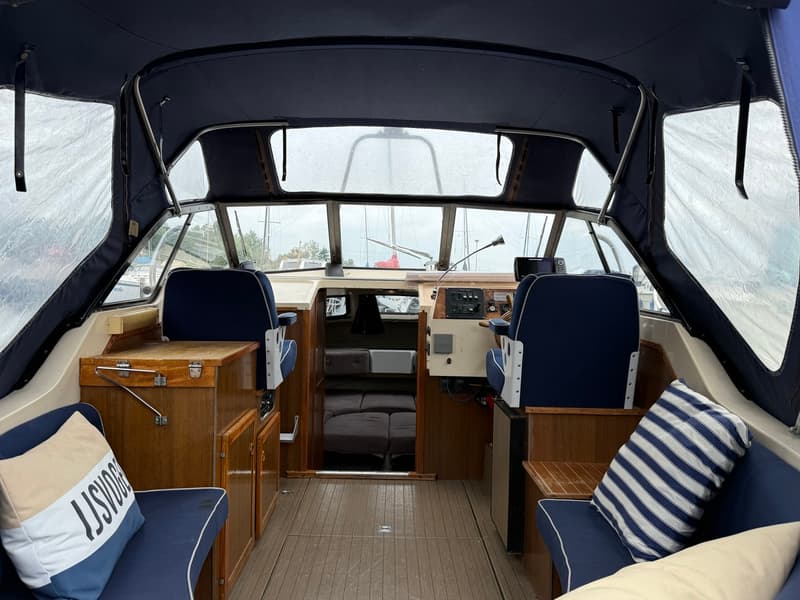 De foto toont het interieur van een boot met een donkerblauwe kap, twee stuurstoelen en een houten vloer. — Joda 7500