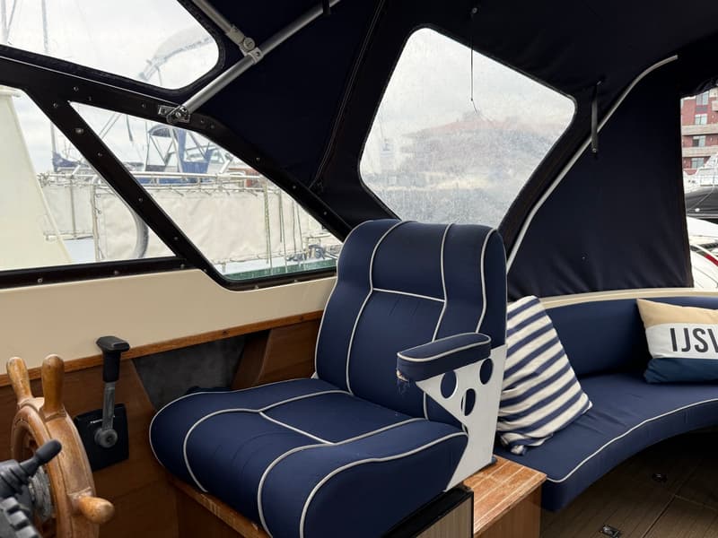 Een blauwe bootstoel met witte biezen en een blauwe bank met kussens zijn zichtbaar in een bootinterieur.