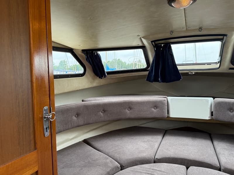 De foto toont het interieur van een boot met een houten deur, grijze kussens en ramen met blauwe gordijnen. — Joda 7500