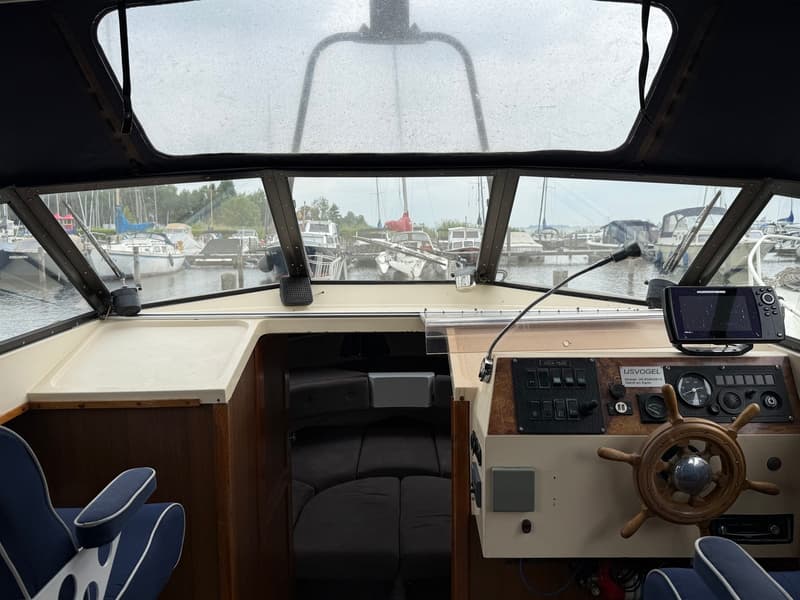 De foto toont het interieur van een boot met een stuurwiel, dashboard en uitzicht op een jachthaven. — Joda 7500