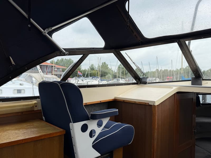 De foto toont het interieur van een boot met een blauw-witte stoel en uitzicht op een haven met andere boten. — Joda 7500