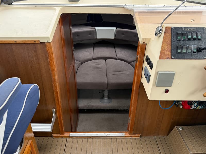 De foto toont het interieur van een boot met een kajuit, een stuurconsole met bedieningspanelen en een blauwe stoel.