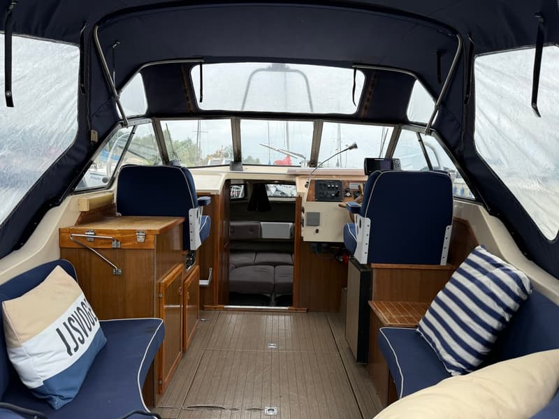 De foto toont het interieur van een boot met een donkerblauwe kap, twee stuurstoelen en een houten vloer. — Joda 7500