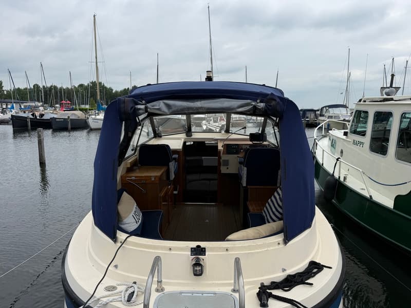 Een boot met een blauwe kap en een houten interieur ligt in een haven met andere boten. — Joda 7500