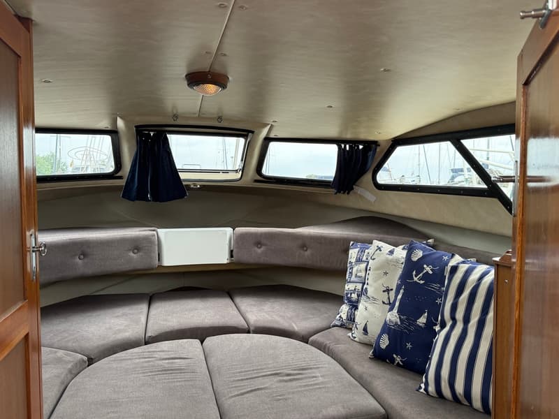 De foto toont het interieur van een boot met een U-vormige zithoek, ramen en nautische kussens. — Joda 7500