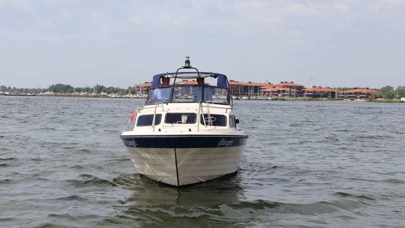 Een witte motorboot met blauwe accenten en de naam "IJsvogel" vaart op water met twee personen aan boord. — Joda 7500