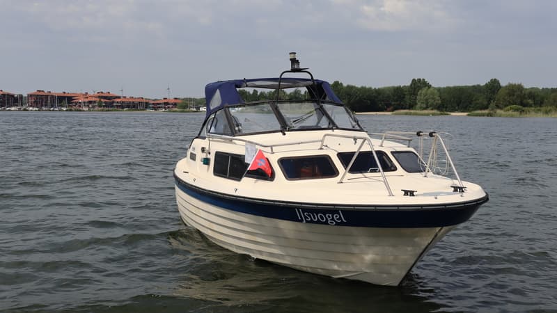 Een crème-witte motorboot met een blauwe streep en de naam "IJsvogel" op de zijkant, drijvend op water. — Joda 7500