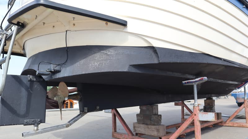De onderkant van een boot met een zwarte romp en een witte bovenkant, staand op een trailer met houten blokken. — Joda 7500