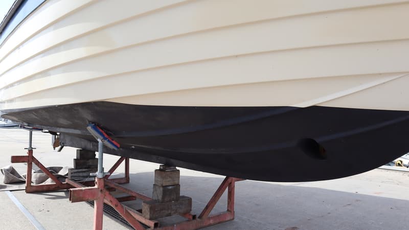 Een boot met een crèmekleurige romp en een zwarte onderkant staat op rode bokken op een betonnen ondergrond. — Joda 7500