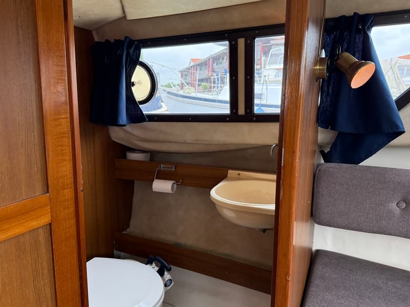 Een interieur van een boot met een toilet, wasbak, ramen met gordijnen en een zitbank. — Joda 7500