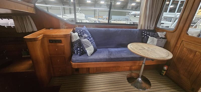 Een interieur van een boot met een blauwe bank, een houten tafel met een kompasroos en houten kasten. — Bach 1050 OK