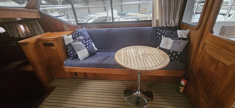 Een interieur van een boot met een blauwe bank, kussens, een houten tafel met kompasroos en een brandblusser. — Bach 1050 OK