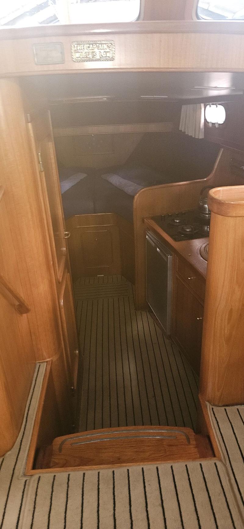 Een interieur van een boot met houten wanden, een kombuis met kookplaat en koelkast, en een slaapgedeelte. — Bach 1050 OK