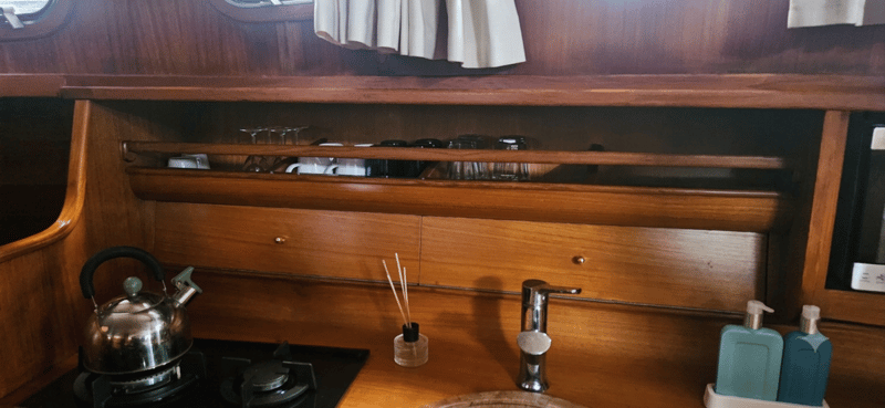 Een houten kombuis met een waterkoker op een kookplaat, een kraan, een geurstokje en twee zeepdispensers.