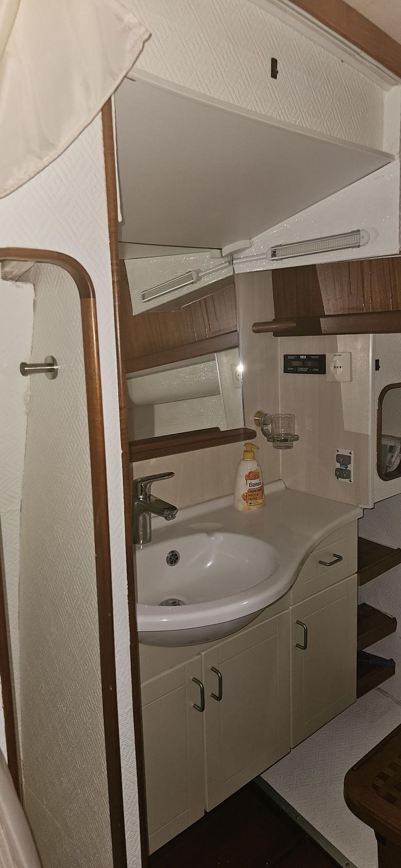 Een badkamerinterieur met een witte wastafel, een kraan, een spiegel en een fles handzeep op een aanrechtblad.
