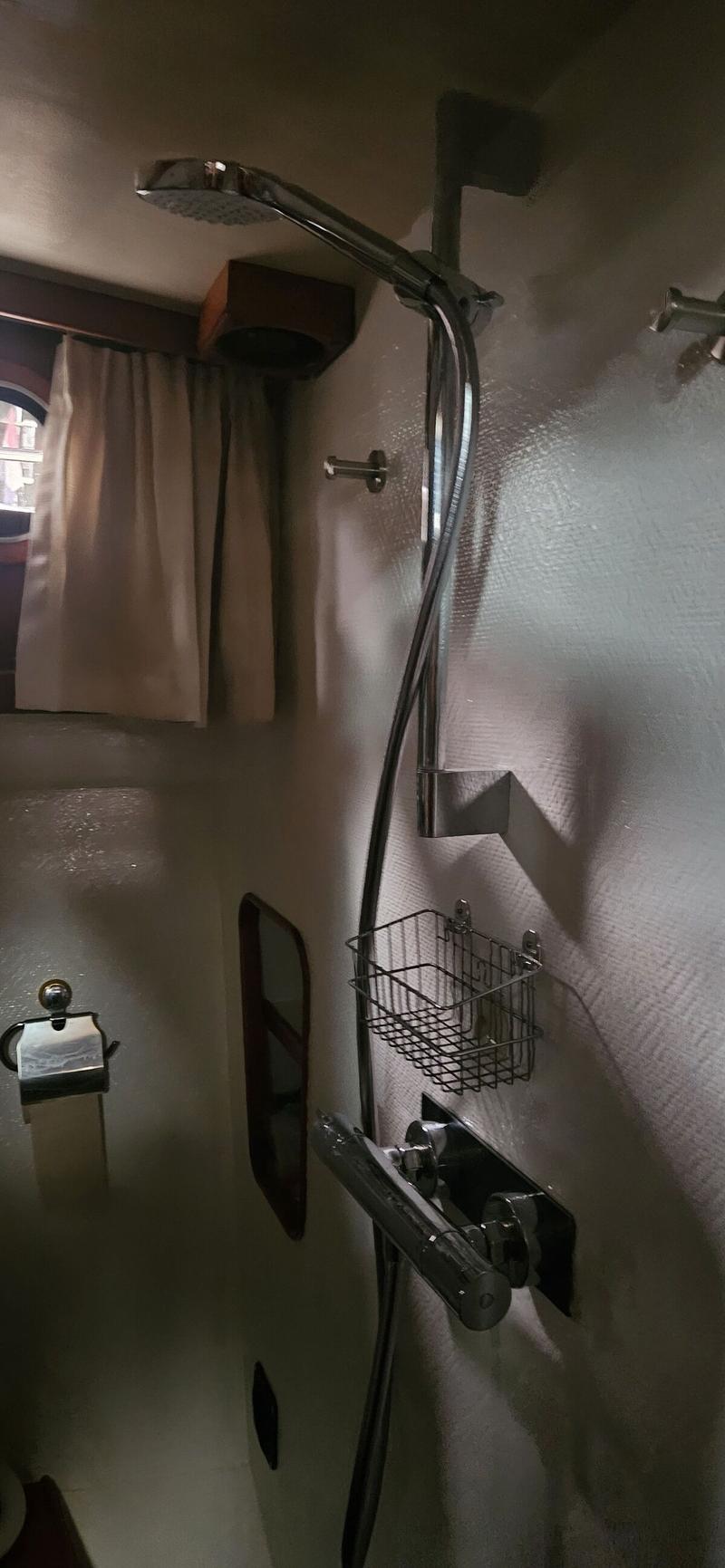 Een douchecabine met een chromen douchekop, mengkraan, zeepbakje en een toiletrolhouder.