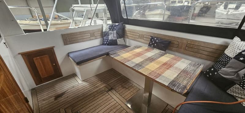 Een interieur van een boot met een houten vloer, een tafel met een geruit kleed, en banken met kussens. — Bach 1050 OK