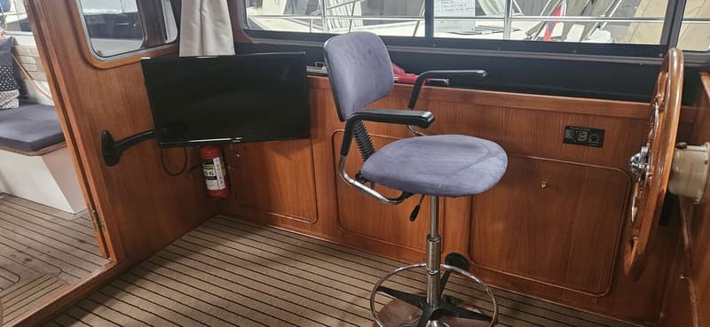 Een interieur van een boot met houten wanden, een gestreepte vloer, een monitor, een brandblusser en een draaibare stoel.