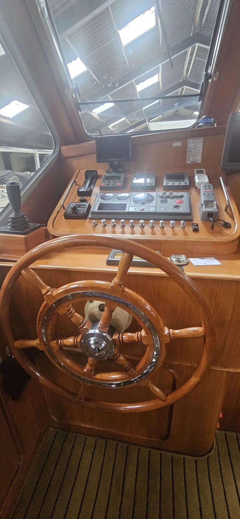 Een houten stuurwiel en dashboard met diverse meters en bedieningspanelen zijn zichtbaar in de stuurhut van een boot.