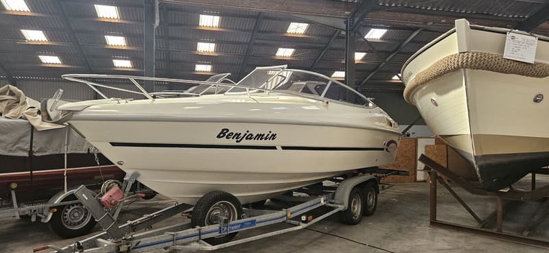 Een witte motorboot met de naam "Benjamin" op de zijkant staat op een trailer in een loods, naast een andere boot.