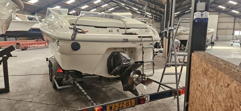 Een witte boot staat op een trailer in een loods, met de achterkant en de buitenboordmotor in beeld. — Cranchi 21 Ellipse