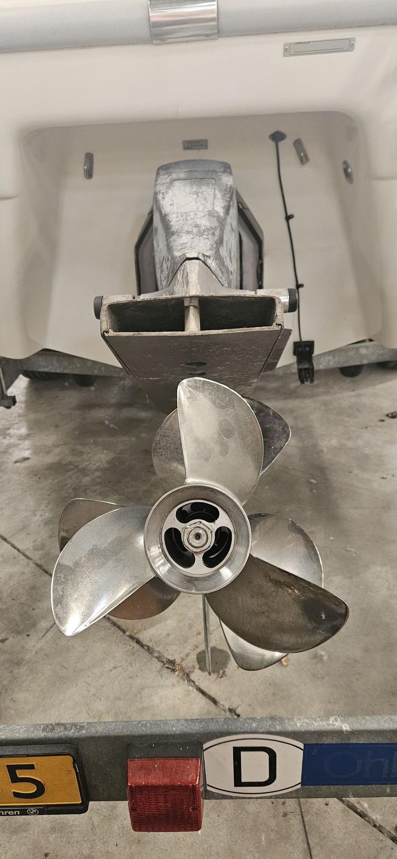 Een close-up van een buitenboordmotor met een driebladige schroef, gemonteerd op een boot die op een trailer staat.