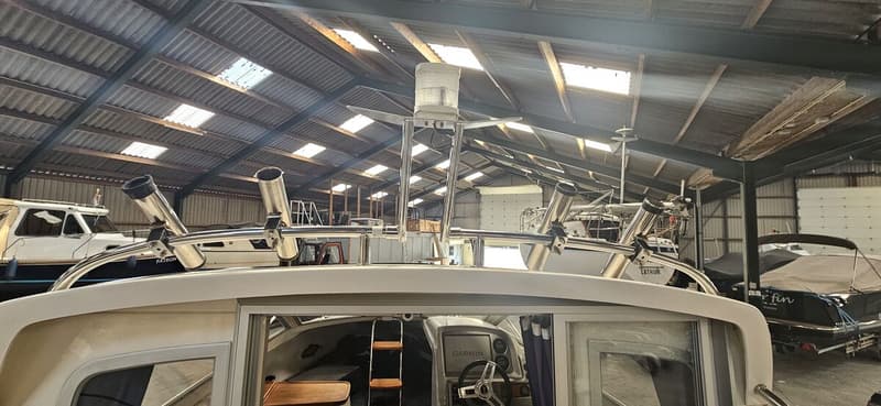 Een boot met een stuurwiel, Garmin-scherm en vishengelhouders, gestald in een loods met andere boten. — Yamarin 68C