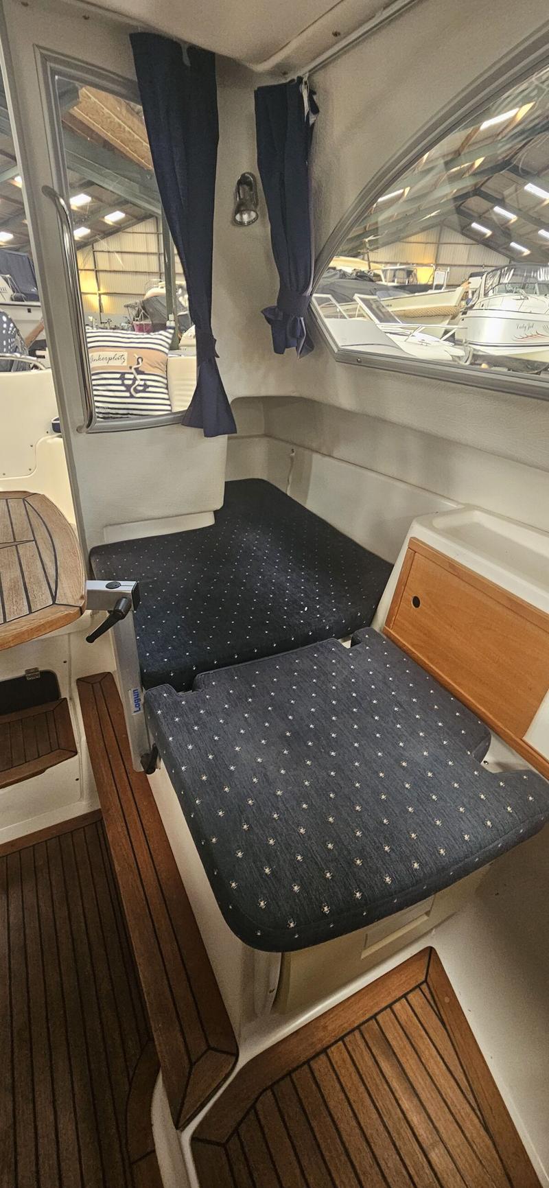 De foto toont een interieur van een boot met donkerblauwe kussens, een houten vloer en ramen met gordijnen. — Yamarin 68C