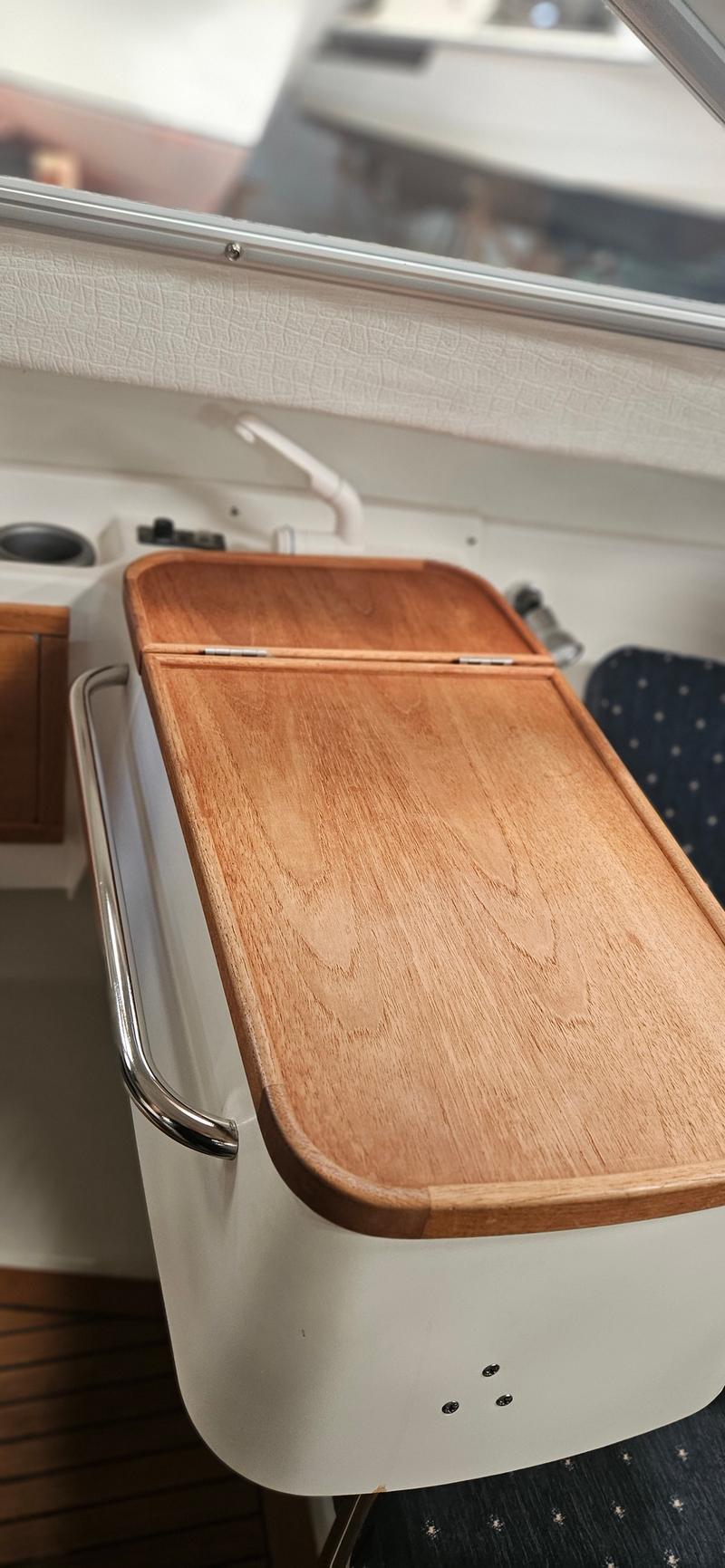 Een houten opklapbare tafel met een metalen handgreep aan de zijkant, gemonteerd op een witte console.