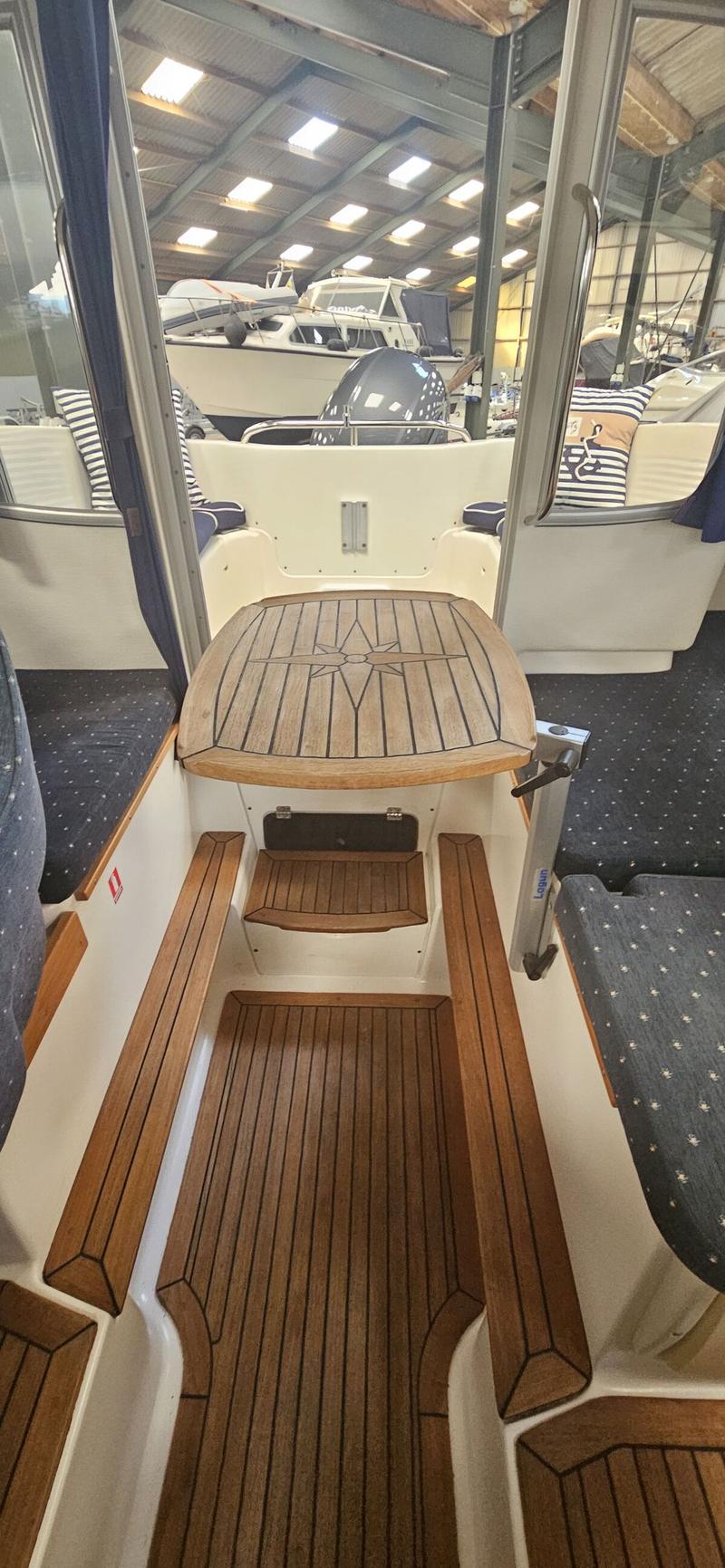 De foto toont het interieur van een boot met een houten tafel met kompasroos en een houten vloer. — Yamarin 68C