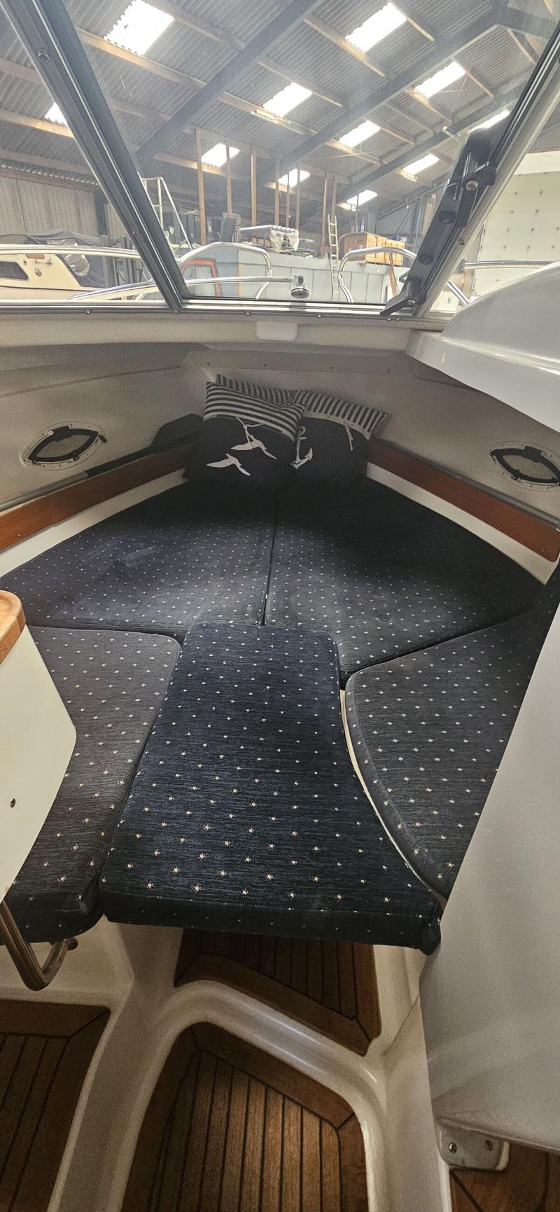 De foto toont het interieur van een boot met donkerblauwe kussens met een stippenpatroon en twee kussens met zeemotieven.