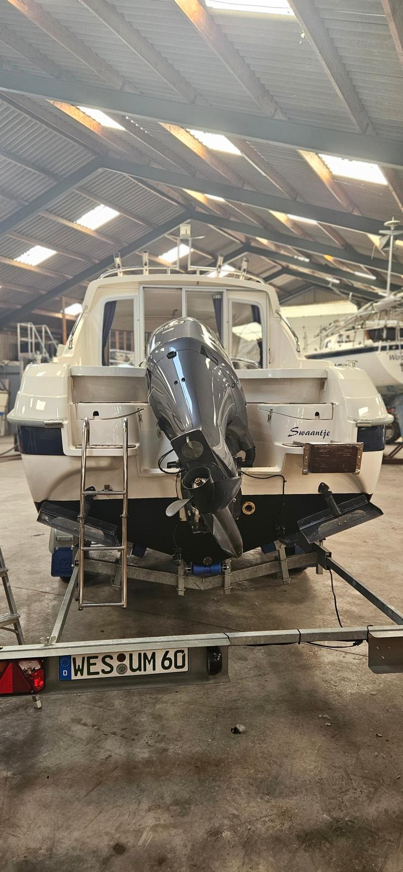 Een witte boot met een grijze buitenboordmotor staat op een trailer in een loods. — Yamarin 68C