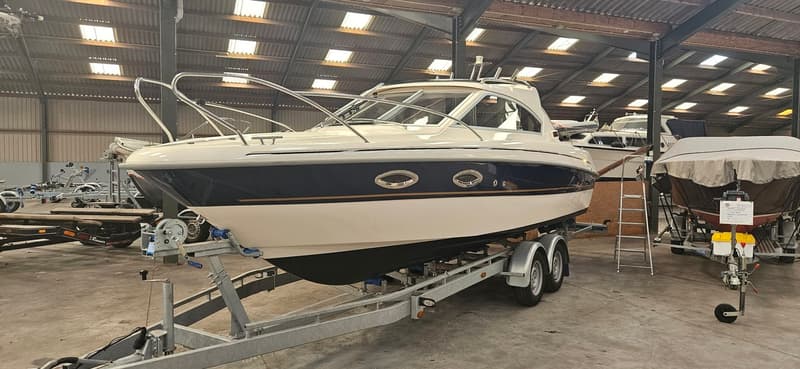 Een witte boot met een donkerblauwe streep en goudkleurige accenten staat op een trailer in een loods. — Yamarin 68C