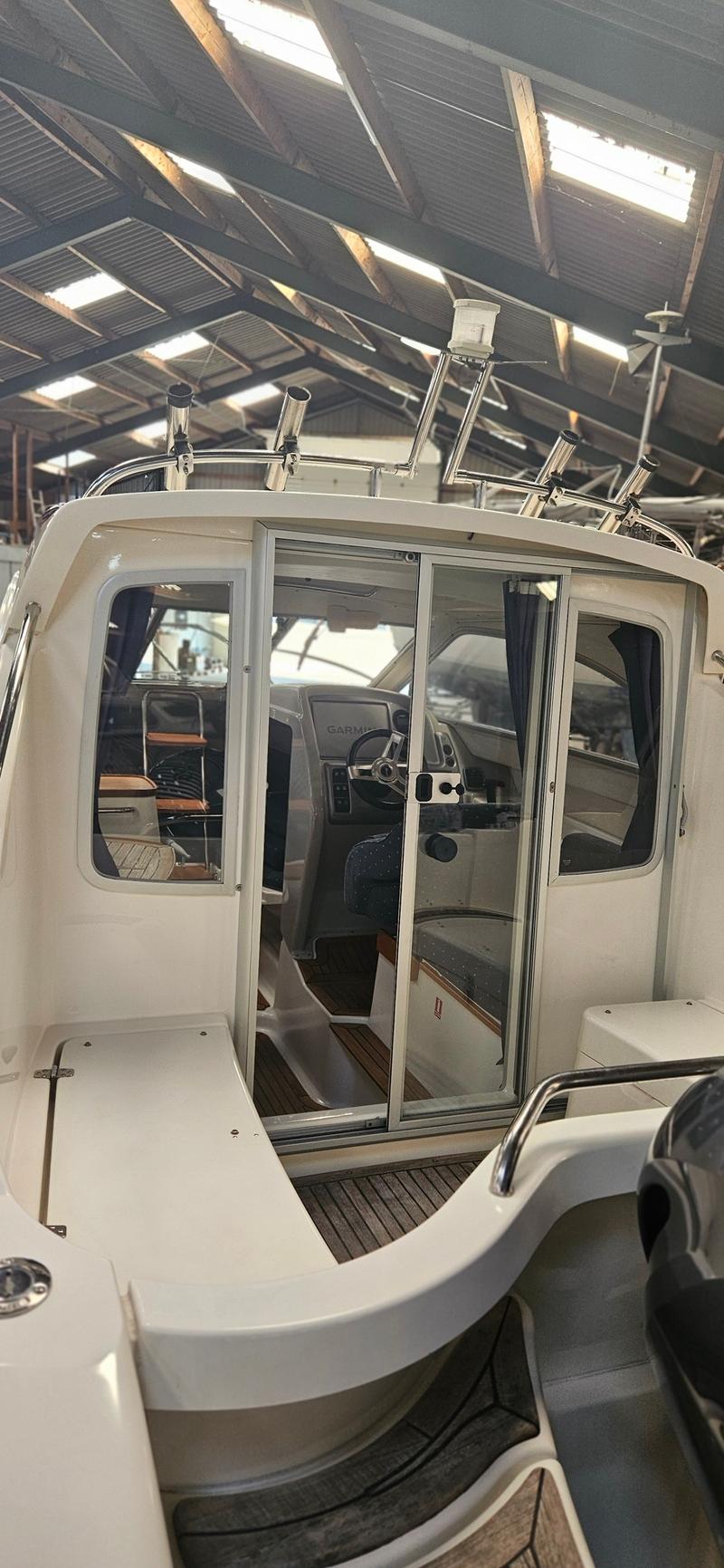 Een witte boot met een stuurhut en schuifdeur, gezien vanaf de achterkant, in een loods met een golfplaten dak. — Yamarin 68C