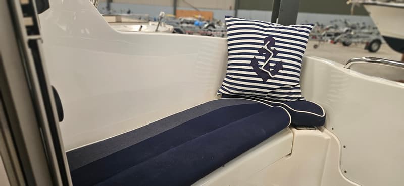 Een detailfoto van een bootinterieur met blauw-wit gestreepte kussens en een ankerpatroon, en blauwe zitkussens.