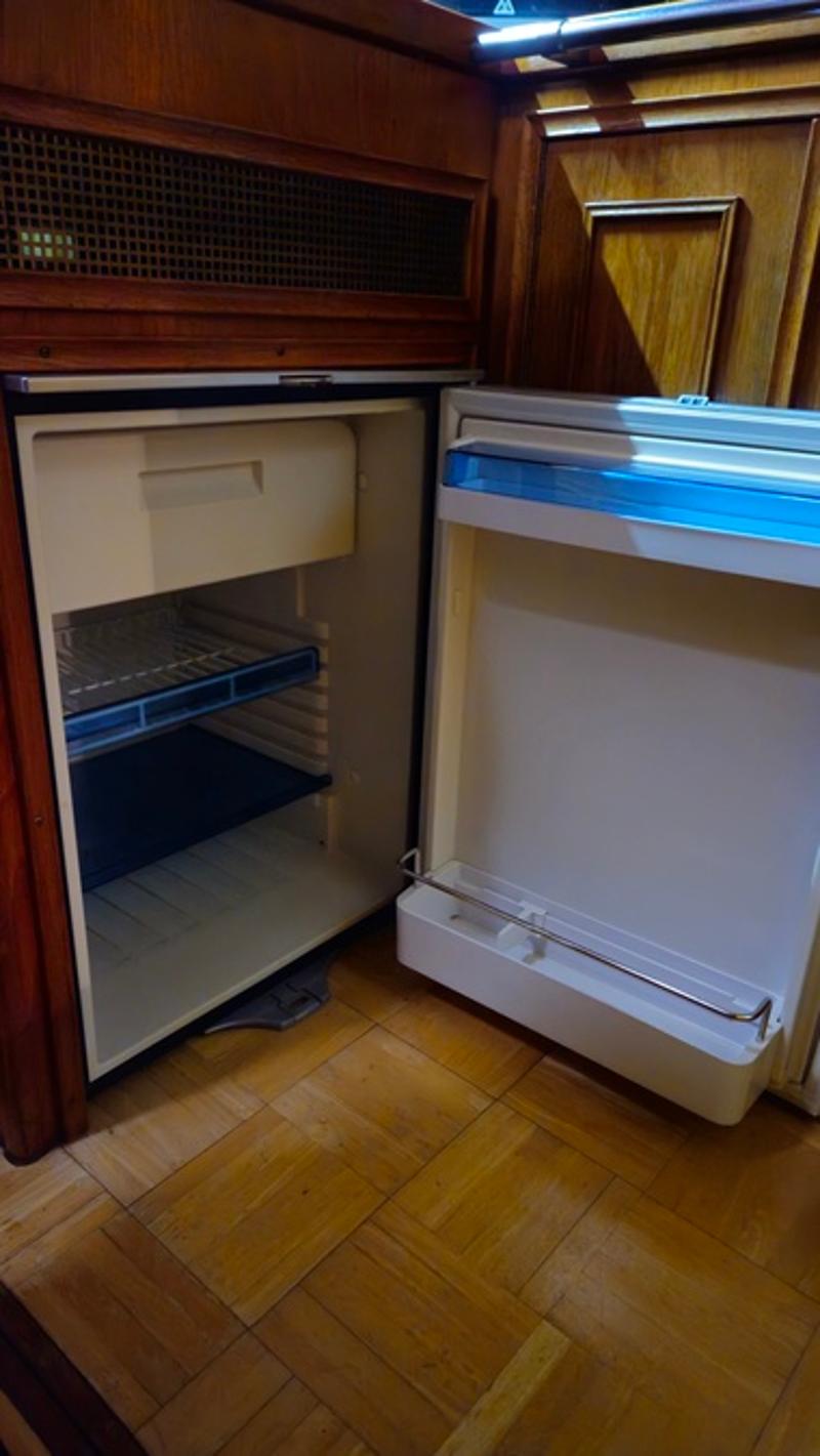 Een open koelkast met een vriesvak en een roosterplank, ingebouwd in een houten interieur met een houten vloer.