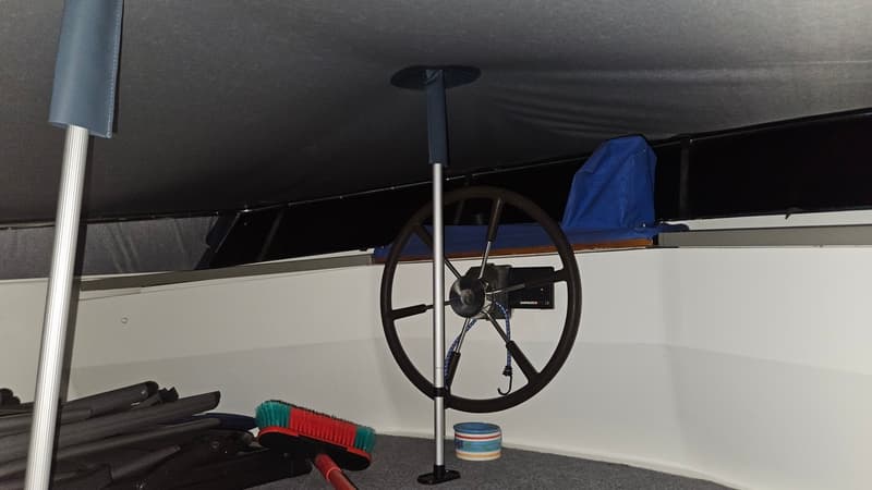 Een stuurwiel met een Shipmate-apparaat is zichtbaar in een boot, met een bezem en opgevouwen stoelen op de vloer.