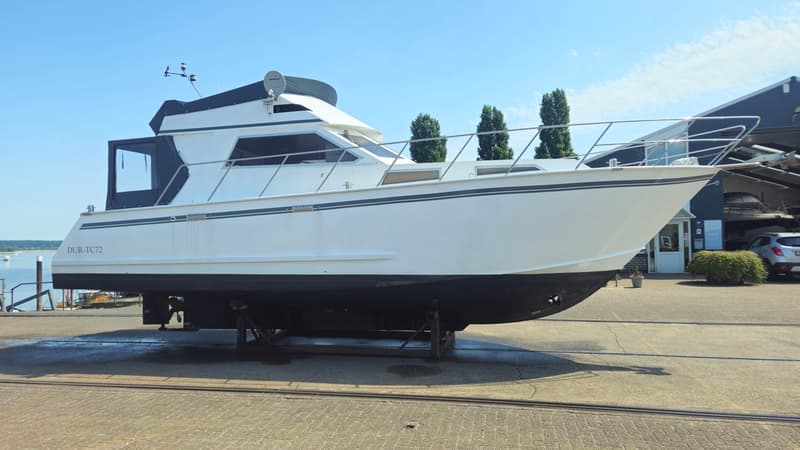 Een witte motorboot met een zwarte romp staat op een trailer op een betonnen ondergrond. — Condor 105 Fly