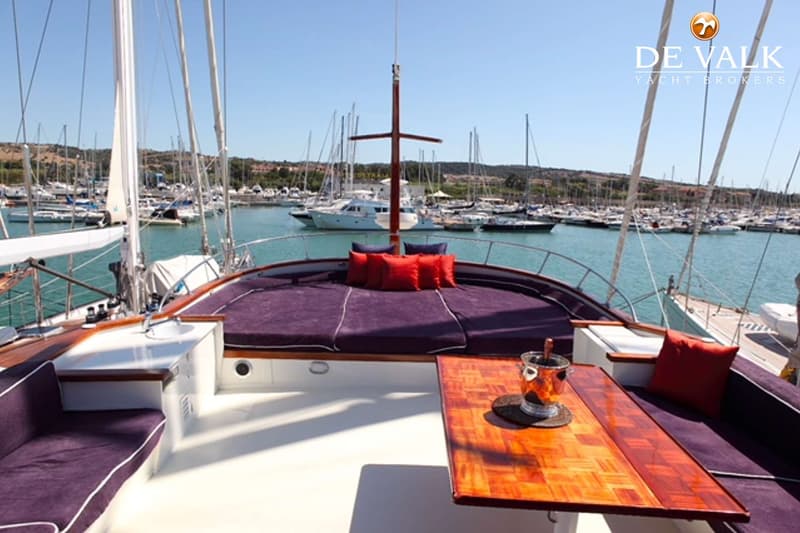 Een bovenaanzicht van een boot met paarse kussens en een houten tafel, liggend in een haven vol met andere boten.