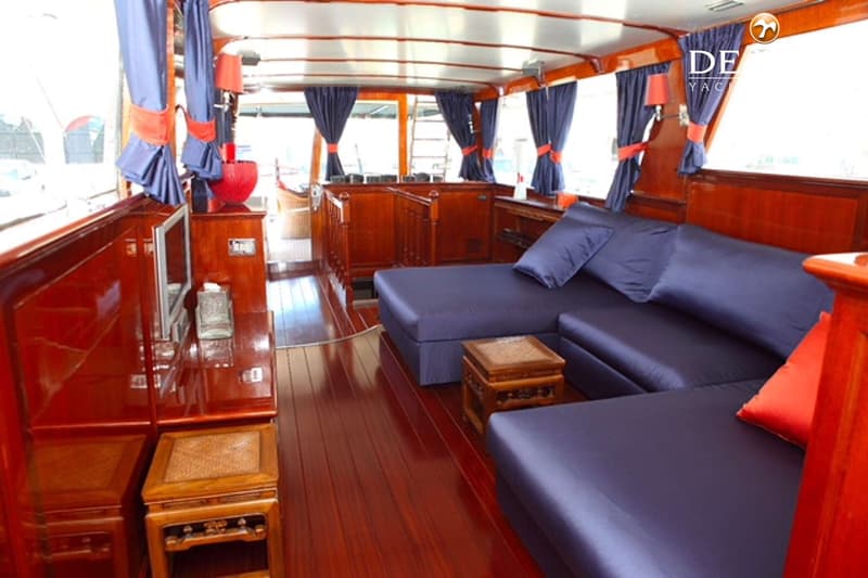 De foto toont een interieur van een boot met glanzend houten wanden en vloer, blauwe banken en gordijnen. — Baglietto Maiorca